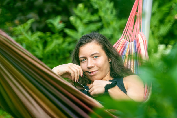 漂亮的女性戴着太阳镜躺在花园的吊床上，放松，选择性的专注图片下载