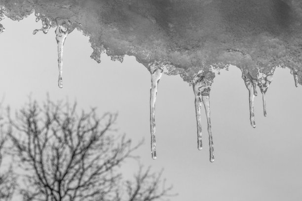 屋顶上挂着雪花和冰柱，背景是木头和灰色天空的黑白照片图片下载