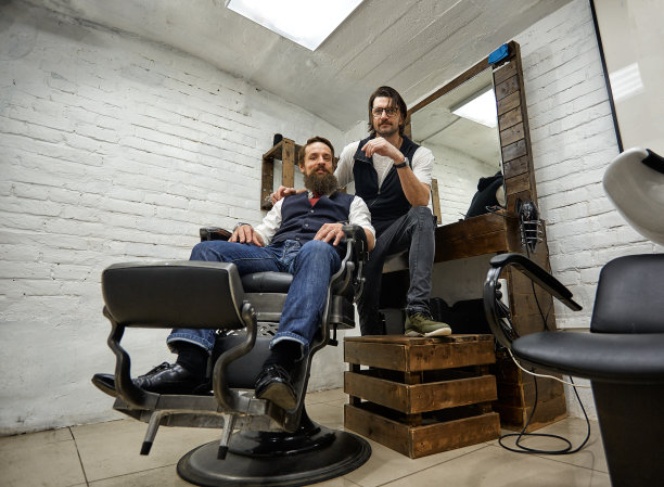 现代理发店里的野蛮人。理发师给留长胡子的男人做发型。发型师用剪刀和梳子做发型图片下载