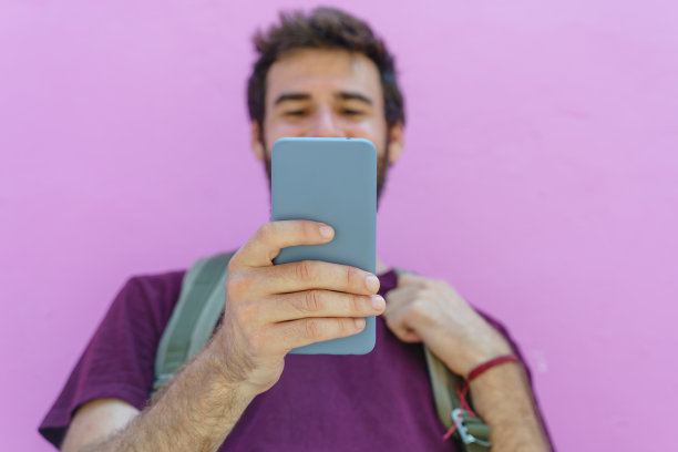 前视图的无法识别的男子拿着手机在粉红色的背景。图片下载