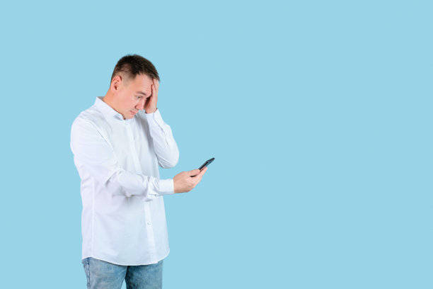 男人悲伤地看着手机屏幕，手放在额头上。蓝色背景,copyspace图片下载