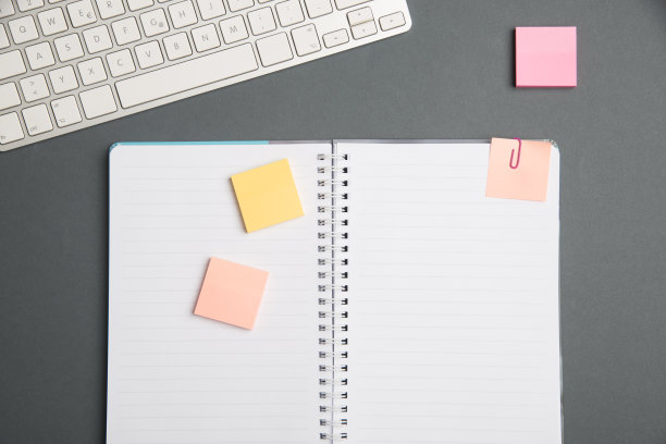 桌上笔记本旁边的键盘和有便利贴的笔。电脑键盘上的桌子上的办公用品和书桌照片。图片下载