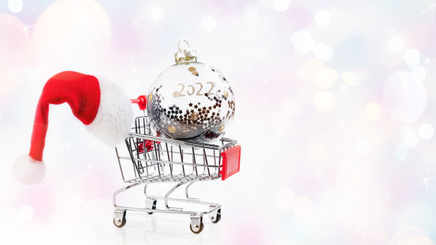 从一个超市的购物车和一个银色圣诞球和圣诞老人的帽子在一个浅色的背景。贺卡，横幅，海报。圣诞家居装饰。圣诞节、冬天、新年的概念。图片下载