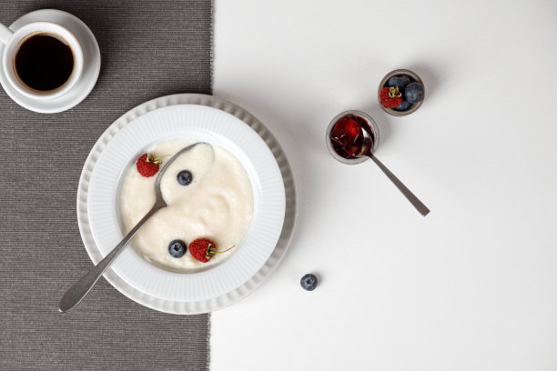 白色的桌子上放着一盘粗面粉粥和一些浆果，一张放着咖啡的灰色餐巾。俯视图图片下载