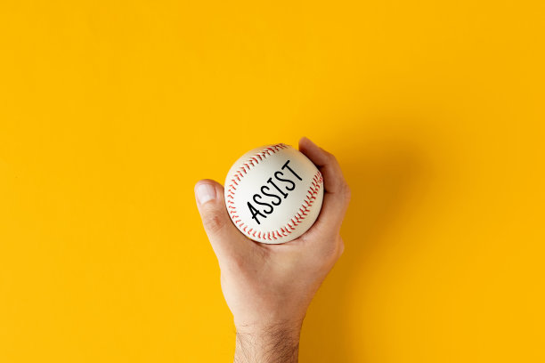 男手拿着黄色背景上写着“协助”的棒球。图片下载