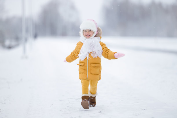 一个快乐的微笑的小女孩穿着暖和的衣服在白雪覆盖的道路上奔跑在寒冷的冬天。前视图。2岁的幼儿。图片下载