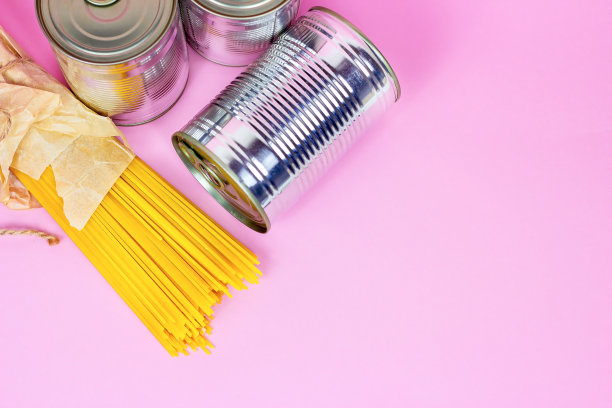 罐头食品，金属罐和黄色意大利面，粉红色背景上有复制空间的意大利面。食品捐赠、配送和慈善理念图片下载
