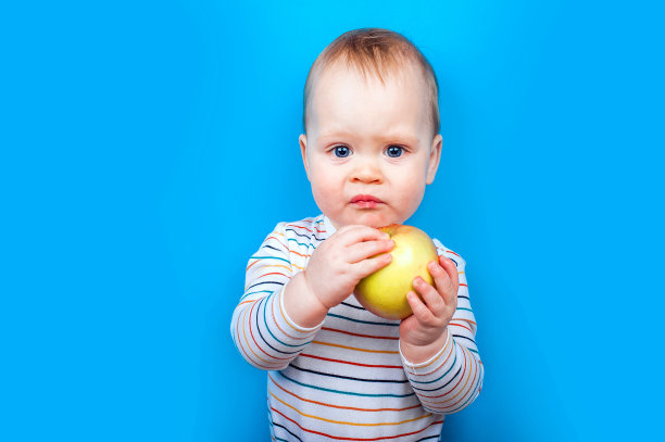 英俊的小男孩与苹果在蓝色的背景。健康饮食观念，儿童先喂，婴儿食品添加剂，过敏图片下载