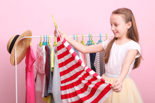 可爱开朗的小女孩选择有地板衣架的衣服。图片下载