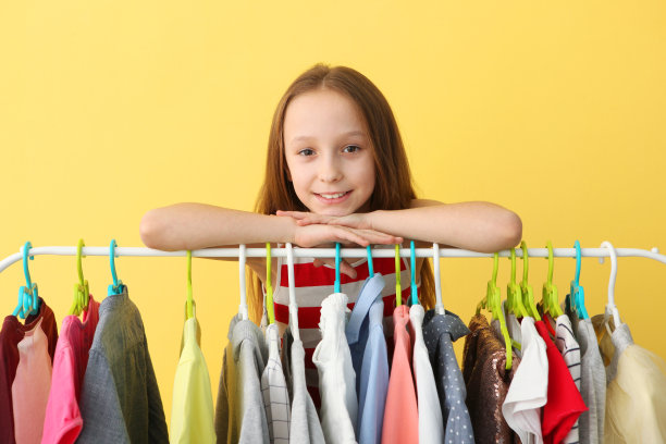 可爱开朗的小女孩选择有地板衣架的衣服。图片下载