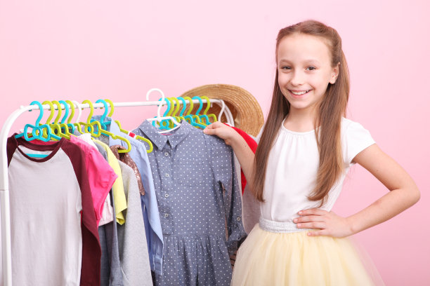 可爱开朗的小女孩选择有地板衣架的衣服。图片下载