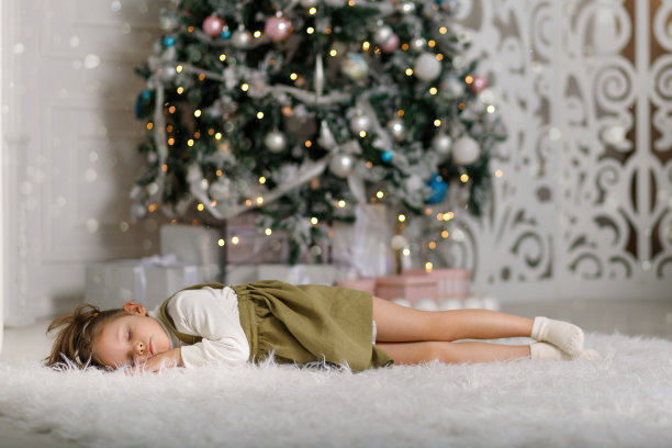 可爱的女孩睡在圣诞树旁边的地毯上图片下载