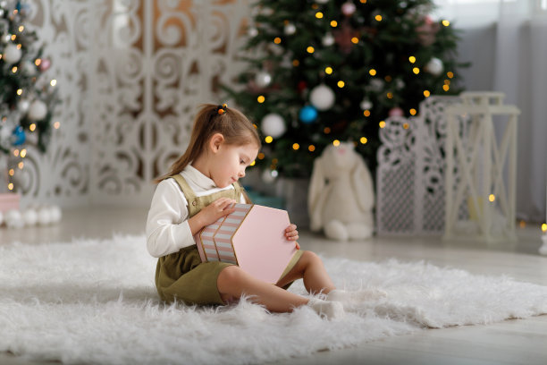 小女孩在圣诞树的背景上打开了一份新年礼物图片下载