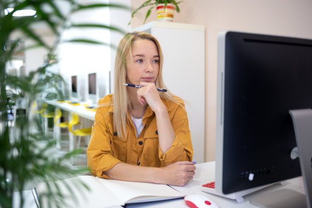 一位年轻的女士坐在办公室的一台电脑前。远程工作的概念图片下载