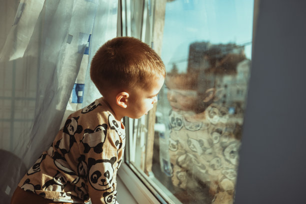 一个蹒跚学步的小男孩从他的房间望向窗外，想念妈妈。孩子的爱，关心和支持。的生活方式。检疫图片下载