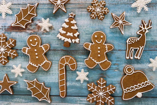 形象喜庆的圣诞设计海报，自制姜饼饼干剪纸形状的圣诞树，拐杖糖，铃铛，冬青树叶，雪花，驯鹿，星星和姜饼人饼干，蓝色，木纹背景图片下载