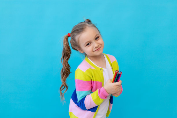 一个可爱的小女孩的肖像，穿着条纹夹克，拿着彩色铅笔。教育和绘画的概念。照片工作室，蓝色背景，放置文本图片下载