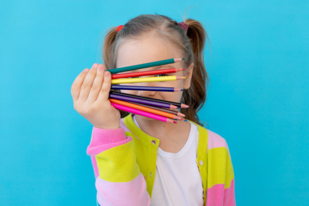 一个可爱的小女孩的肖像，穿着条纹夹克，拿着彩色铅笔。教育和绘画的概念。照片工作室，蓝色背景，放置文本图片下载