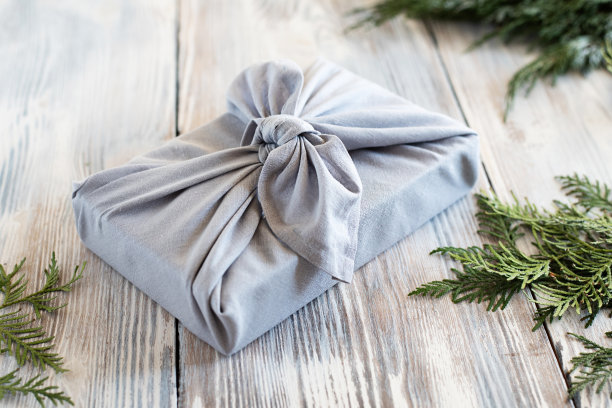 用可重复使用的布料包装的礼物，背景是白色的木质。图片下载