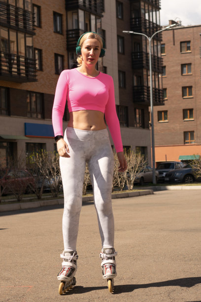 戴着耳机的年轻女子运动员在城市运动场上滑旱冰。积极的生活方式爱好轮滑图片下载