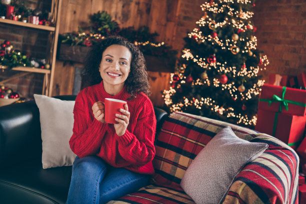 迷人的漂亮女士照片坐在舒适的沙发拿杯子咖啡享受圣诞夜穿毛衣在室内装饰的家图片下载