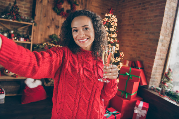 照片迷人的积极成熟的女人穿红色毛衣微笑庆祝新年钉自拍照喝酒在室内的房子家房间图片下载