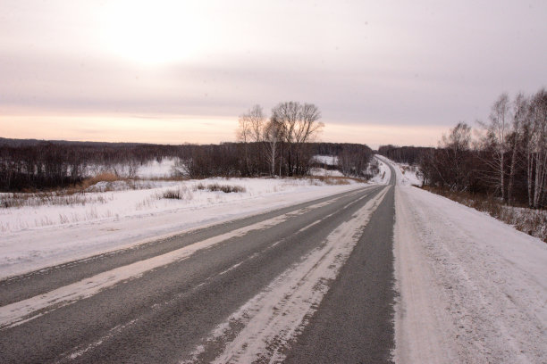 在柏油路的拐弯处，路边的雪堆延伸到白雪覆盖的田野，迎接夕阳。图片下载