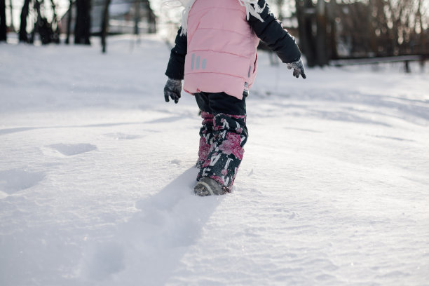 孩子在冬天走路。在阳光明媚的霜冻日子里，小女孩穿着暖和的冬装在森林里爬上雪道图片下载