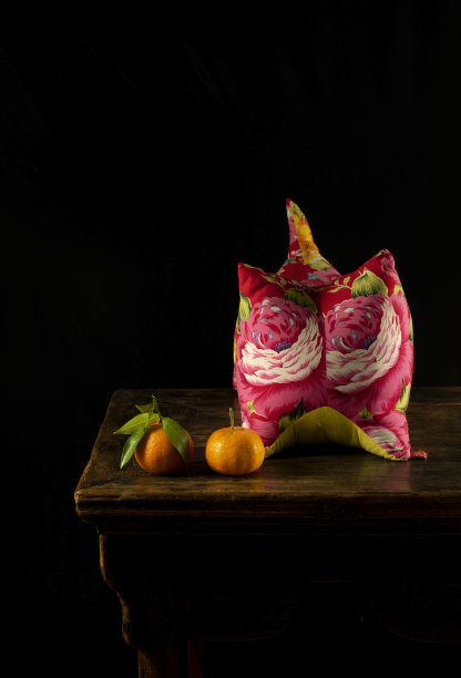 中国民族风格静物画，红色老虎枕，木桌上的陈皮水果，靠黑墙图片下载