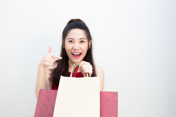 亚洲美女微笑着指着购物袋，开心地购物。一个购物狂。“黑色星期五”。图片下载