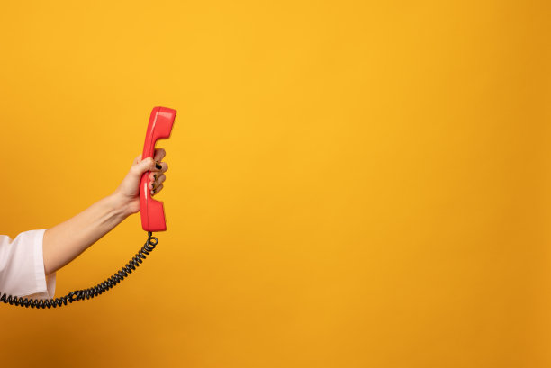 特写的妇女持有红色有线电话听筒在黄色的背景上，文字的空间。热线的概念图片下载