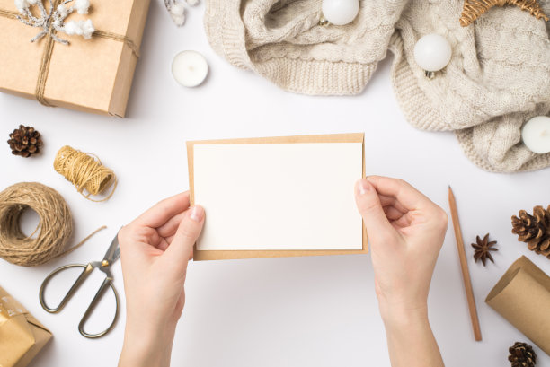 第一个人顶视图照片，手拿卡片信封，礼盒，毛衣，圣诞树，球，工艺品，锥，八角，蜡烛，剪刀，线轴，在孤立的白色背景与copyspace图片下载