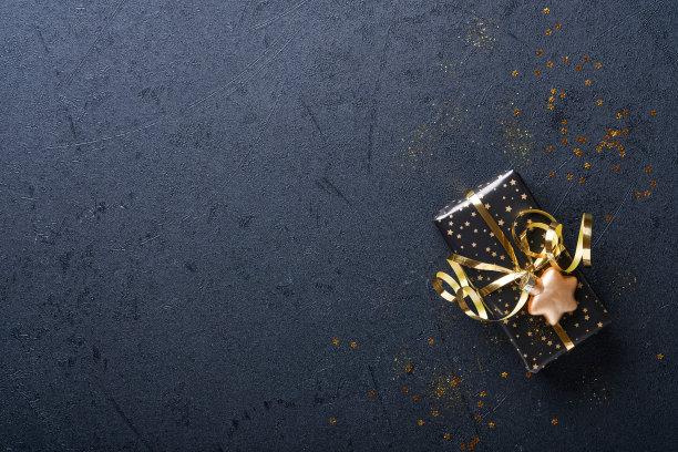 假日礼品盒或礼品带，金色的纸屑和金色的小玩意在黑色的背景上。神奇的圣诞贺卡。圣诞装饰。边界设计。模拟。前视图。图片下载