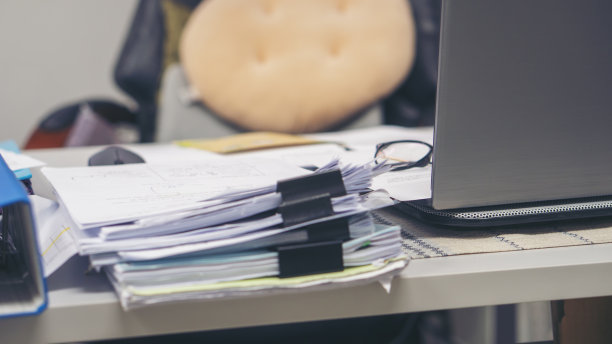 笔记本电脑和年度报告的堆叠，为会计或簿记计划预算和税收。电脑和总结报告放在蓝色的木桌上，在家里的工作空间。家庭办公桌的概念。图片下载