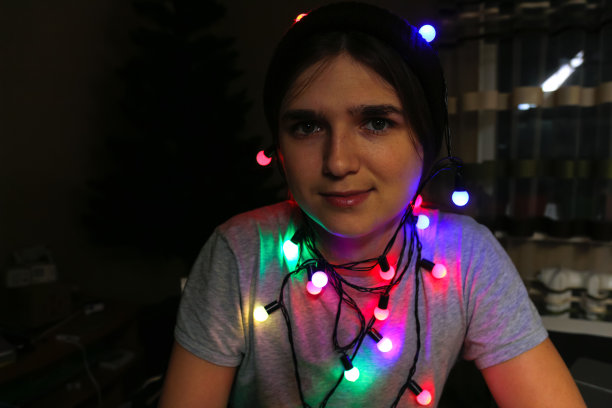 圣诞晚会。时髦的年轻女人庆祝圣诞节和看着相机。年轻人在五颜六色的彩灯下玩寒假。裹在彩色圣诞彩灯中的女人图片下载