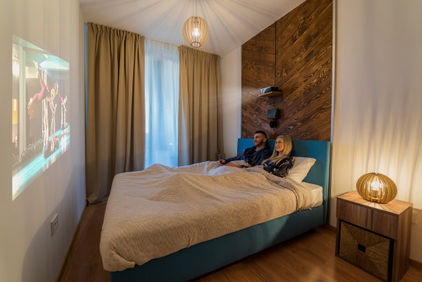 一对年轻的夫妇躺在卧室的床上，看着墙上的电影，看起来很开心。图片下载