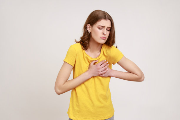 穿着黄色T恤的棕发女性，闭着眼睛触摸胸部，感到突发剧痛，有心脏病发作的风险，紧急情况图片下载