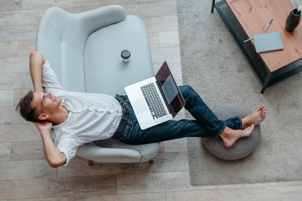 一个年轻人拿着一杯咖啡和一台笔记本电脑坐在沙发上图片下载