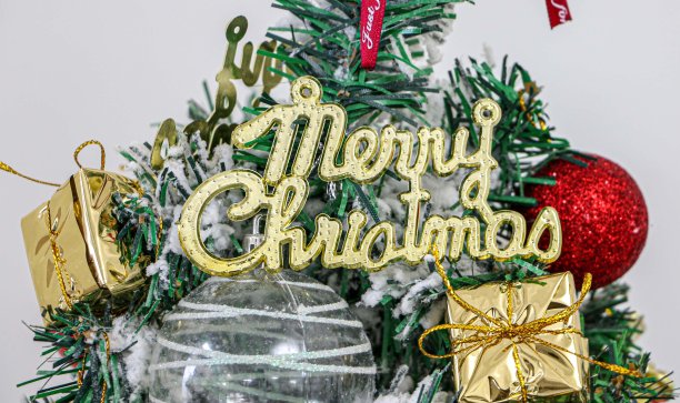 圣诞快乐祝福在风格化字体装饰圣诞树与红色和白色的小玩意，和黄金包装的礼物图片下载