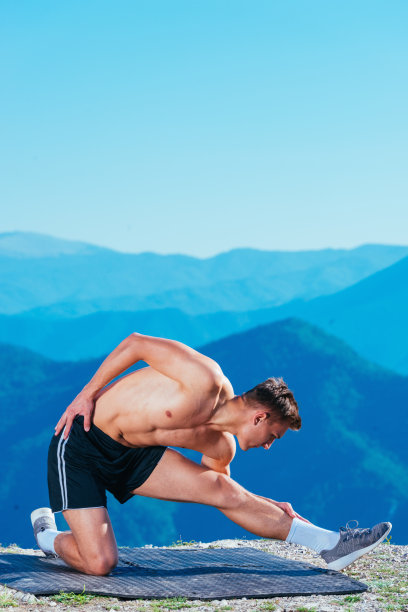 英俊的运动员(运动员)在山顶伸展身体准备锻炼，山上有令人惊叹的风景。图片下载