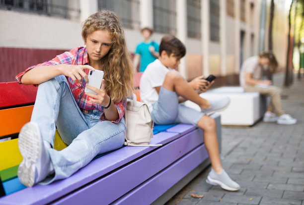 十几岁的女孩和男孩拿着智能手机坐在长椅上图片下载