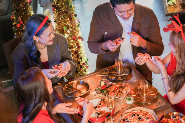 美丽的亚洲朋友男女聚会庆祝。女人在桌子上提供披萨，小吃和饮料。幸福朋友平安夜庆祝会晚宴美食香槟。图片下载