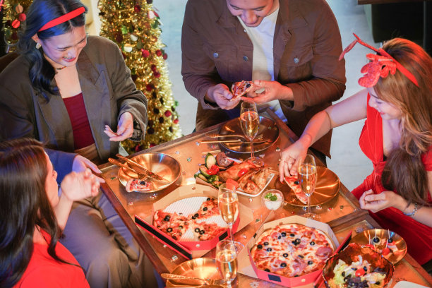 美丽的亚洲朋友男女聚会庆祝。女人在桌子上提供披萨，小吃和饮料。幸福朋友平安夜庆祝会晚宴美食香槟。图片下载