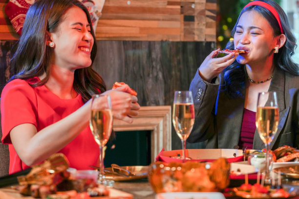 美丽的亚洲朋友女性聚会庆祝。女人在餐桌上吃披萨，还有零食和饮料。幸福朋友平安夜庆祝会晚宴美食香槟。图片下载