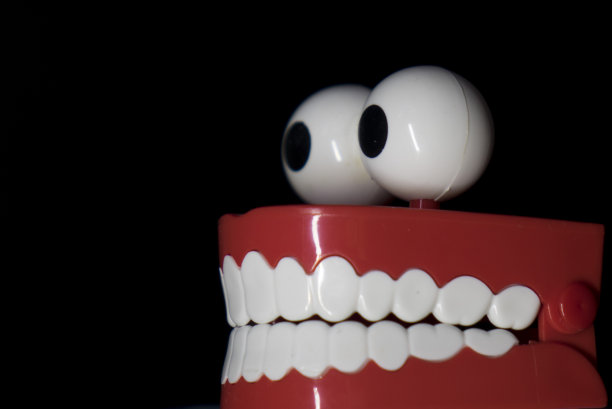 一个微笑的玩具假肢，白色的牙齿和大眼睛孤立在黑色背景下。图片下载