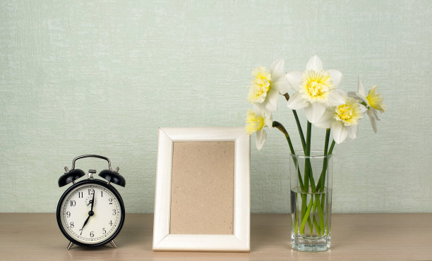 花瓶里的水仙花，动作捕捉照片的竖框，靠在绿松石墙上的桌子上的机械闹钟图片下载