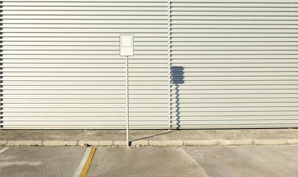 白色的空标志在一个白色铝包覆墙前的一根杆子上。混凝土人行道和路边。图片下载