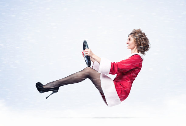 年轻快乐的女孩穿着红色圣诞老人的衣服，手里拿着方向盘开车，周围是雪图片下载