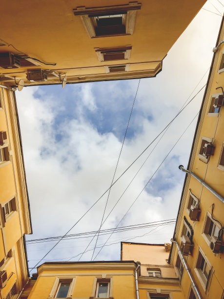 紧密建造的房屋的黄色墙壁的底部视图。窄小的庭院也叫井。俄罗斯莫斯科的一幢老建筑。图片下载