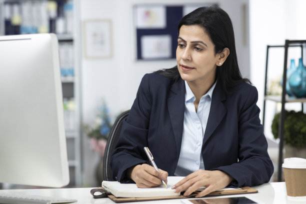 迷人的女商人坐在室内办公室的桌子上，工作。库存图片图片下载